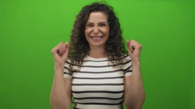 Omuz hizasında çıplak yumruklu çizgili bir gömlek giyen ve yeşil bir stüdyoda gülümseyen bir kadın..