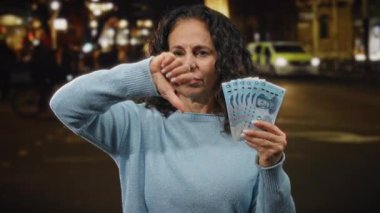 Bir kadın elinde Yuan banknotları tutarken, gece bir şehir caddesinde onaylamadığını belirterek, Çin para birimiyle mali hoşnutsuzluğu ve kentsel ambiyansı vurguluyor..