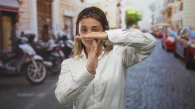 Elleri ve şaşı yüzüyle mobiletler ve arabalarla dolu bir kaldırım taşı sokakta el kol hareketi yapan bir kadın..