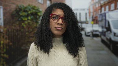 Tuğla binalar ve park halindeki beyaz minibüslerle dolu bir caddede kırmızı gözlüklü bir kadının gözleri şaşı kaldı..