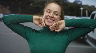 Şehir caddesinde yeşil kazaklı, çenesine yakın elleri olan gözlük takan kadın; mutluluk sevinç güveni sıcaklığı.