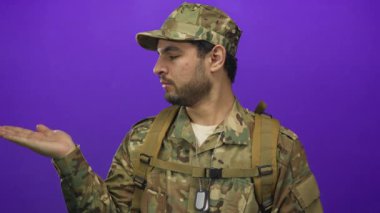 Kamuflaj üniformalı, künyeli bir adam avucunun içini açıp stüdyoda eline bakıyor..