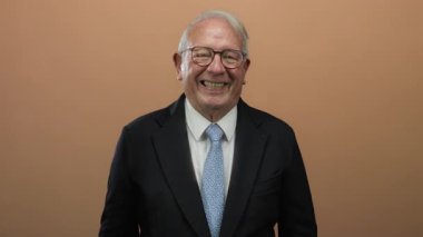 Üst düzey bir adam izole edilmiş kahverengi bir arka plana gülüyor ve alkışlıyor. Profesyonel bir ortamda neşe ve başarı taşıyor..