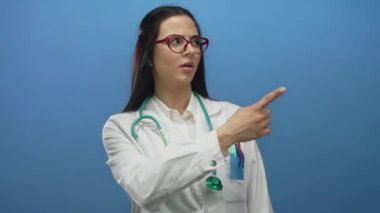 Steteskoplu ve kırmızı gözlüklü genç İspanyol kadın doktor mavi duvarın arkasında farklı yönleri göstererek seçim yapmayı ya da karar vermeyi öneriyor..
