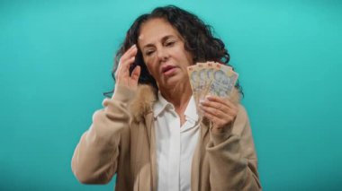 Romen banknotlarını elinde tutan orta yaşlı bir kadın mavi bir arkaplana karşı endişeli bir ifadeyle.