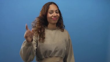 Kadın, gülümseyen ve nişan alan el kamerasıyla mavi stüdyodaki kamerayı işaret ediyor; güven bağlantısı.