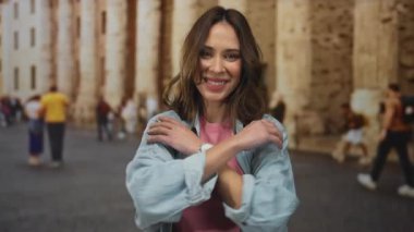 Genç İspanyol kadın canlı bir şehir caddesinde kendini kucaklıyor. Etrafı antik taş binalar ve çeşitli yayalarla çevrili..