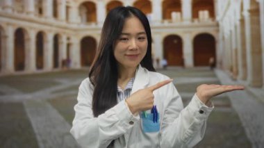 Üniformalı genç Çinli kadın bilim adamı eski bir kasaba avlusunda mutlu bir şekilde el kol hareketi yaparak tarihi bir ortamda yenilik ve uzmanlık öneriyor..