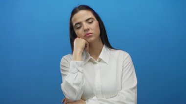 Beyaz gömlekli, mavi bir duvara yaslanan kadın bıkkınlık ve bıkkınlık gösteriyor..