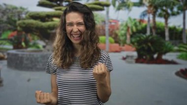 Çizgili tişörtlü genç İspanyol kadın parlak güneş ışığı altında gözleri kapalı yumruklarını sıkıyor; heyecan.