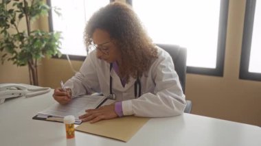 Beyaz önlüklü kadın doktor elinde ilaç şişesi ve klinikteki panoya steteskopla yazı yazıyor..