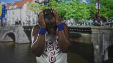 ABD forması ve bileklikleriyle Amsterdam 'da bir kanal köprüsünde el ele tutuşan adam hayal kırıklığı yalnızlığının yansıması..