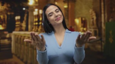 Kilise ortamında davetkar bir ifadeyle el kol hareketi yapan, mavi bir bluz giyen, sıcak ve sıcak bir karşılama yapan bir kadın..