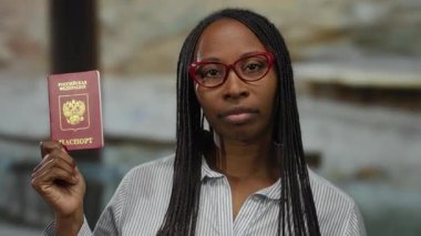 Açık havada elinde Rus pasaportu olan bir kadın şehir ortamında kimlik gösteriyor. Gözlük ve çizgili gömlek giyiyor. Resmi belge sunumunu vurguluyor..