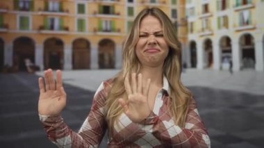 Kadın, kalabalık şehir meydanında güneş ışığı altında parmaklarıyla burnunu sıkıyor; tiksinti reddetme nefreti.