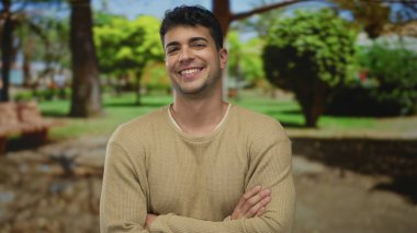 Adam parkta kollarını kavuşturuyor. Genç, İspanyol asıllı, güler yüzlü bir adam havası var..