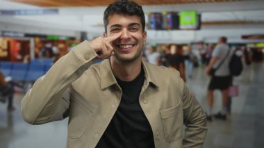 Adam parmaklarını burnuna yakın tutuyor ve havaalanının içinde dokunuyor. İspanyol bir genç, terminal tahtasının yanında durup nazikçe gülümsüyor..