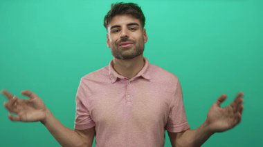 Avuç içi açık pembe tişörtlü bir adam stüdyoda yeşil arka plana karşı nazik bir gülümseme..