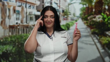 Güneşli bir günde palmiye ağaçlarıyla kaplı bir caddede pembe jilet tutan kadın, şehir hayatı ve kendine güveni somutlaştırıyor..