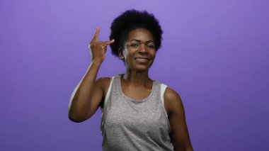 Kadın, güven ve ifadeyi vurgulayan münferit mor arka plana gülümserken kaya hareketi yapıyor.