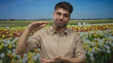 Gözlük takan adam, ormanda canlı çiçekler üzerinde gülümseyen yüzle el ele tutuşuyor; büyüme bolluğu sevinci.