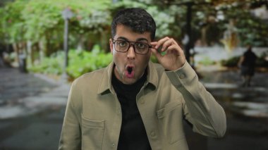 Genç Latin asıllı bir adam sokakta ağzını açık gösteriyor. Gözlüklü bir adam, bilinmeyen bir olayı fark ediyor..