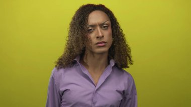 Mor gömlek giyen transseksüel bir kadın sarı bir stüdyoda orta parmağını gösterirken sıkılmış yumruklarını kaldırıyor..
