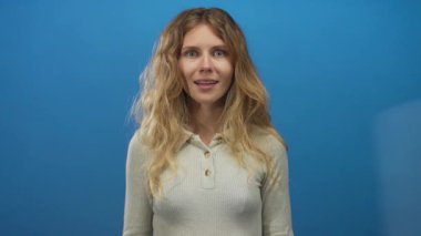 Stüdyo ortamında gülümseyen, mavi arkaplan portresi üzerinde diş telleri olan genç sarışın bir kadın..