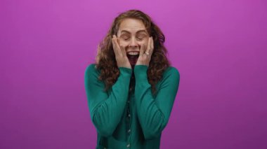 Yüzünde elleri olan bir kadın pembe arka plana karşı heyecanını ifade ediyor, neşe ve şaşkınlık taşıyor..