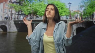 Avuç içleriyle omuz silken ve Amsterdam caddesinde kanal köprüsü üzerinden kot gömlek ve sarı kolsuz bluz giyen bir kadın el kaldırdı..