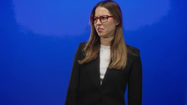 Kırmızı gözlüklü genç İspanyol kadın mavi stüdyoda burnunu ve yüzünü buruşturuyor; iğrenme reaksiyonu.