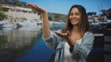 İspanyol kadın avuçlarıyla gülümsüyor liman iskelesinde kot gömlek, görünür eller ve tırnaklar giyerek jest yapıyor..