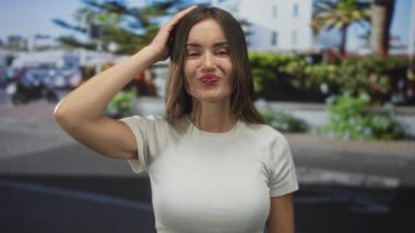 Güneşli şehir sahnesinde elini sallayan genç İspanyol kadın, ileriye bakarken sıcak bir şekilde gülümsüyor; mutluluk..