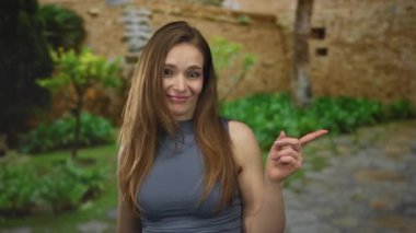 Taş duvar ve yeşillik zemin ile eski kasabanın kaldırım taşı caddesinde kolsuz üst işaret parmağı olan bir kadın..