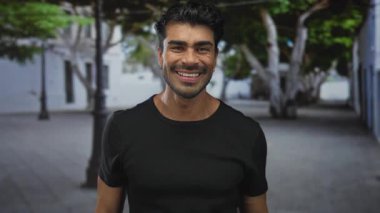 Siyah gömlekli bir adam gülümsüyor ve bir şehir caddesinde bağırarak bir jest yapmak için kıt kanaat ağlıyor..