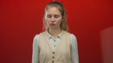 Kadın, genç bir sarışının kırmızı bir arkaplana karşı yakın bir portrede reddetme ifadesi sergilediği bir stüdyo sahnesinde cesur bir hareketle elini kaldırır..