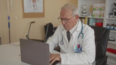 Klinikte dizüstü bilgisayarda çalışan kıdemli doktor hastane içinde odaklanmış profesyonel bir ortam gösteriyor..