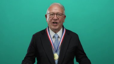 Kıdemli takım elbiseli adam yeşil arka planda madalyayla kutlama yapıyor, başarıyı ve başarıyı vurguluyor..