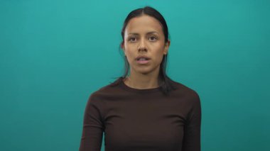 Kahverengi gömlekli İspanyol kadın, izole edilmiş yeşil duvar arka planına karşı duygusal hareketler yapıyor..