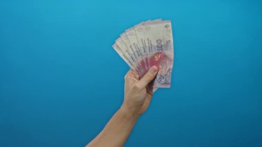 Arjantin pesolarını elinde tutan adam elinde banknotlarla mavi arka planda, beyaz erkek finans ve zenginlik kavramını gözler önüne seriyor..