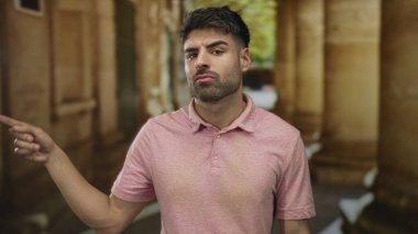 Pembe gömlekli genç adam eski kasabadaki yıpranmış taş binayı işaret ediyor..