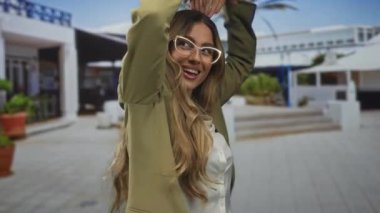 Spor ceket giyen ve gözlük takan bir iş kadını açık hava meydanında elleri ile kalp hareketi yapıyor. Mutluluğu seviyorum..