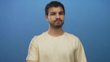 Latin asıllı genç adam işaret parmağını ciddi bir ifadeyle mavi stüdyoda kameraya doğrultuyor..