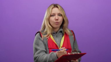 Volunteer woman writing notes on clipboard with purple background, dressed in red vest, emphasizing community service and engagement.