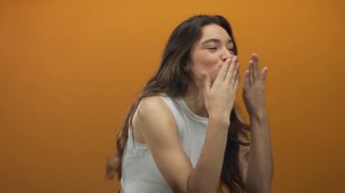 Portakal rengi stüdyoda gülümseyen ve öpücük jesti yapan çıplak omuzlu genç İspanyol kadın şefkatli..