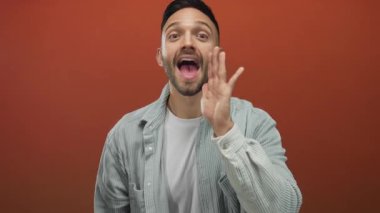 Genç adam coşkuyla bağırıyor elleri çerçeveli canlı turuncu arka plana karşı heyecan ve enerji taşıyor..