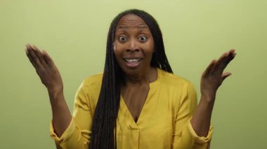 Sarı gömlekli, sarı bir duvara karşı şaşırdığını ifade eden örgülü bir kadın stüdyo ortamında canlı duygular ve saç stili sergiliyor..