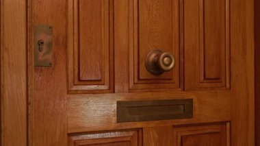 Pirinç saplı ahşap kapı ve güneşli ışığın altında açık posta yuvası detaylı doku ve tasarım gösteriyor..