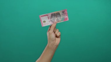 Endonezya 'nın yeşil duvara karşı el ele tutuşması, erkek kolunun yer aldığı, basit bir geçmişe sahip canlı para biriminin ele geçirildiği izole bir ortamda finansal odak noktasını taşır..