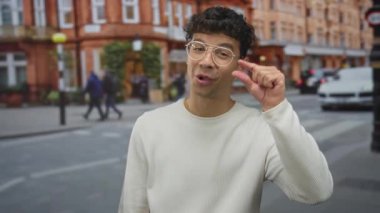 Genç İspanyol adam gün ışığında şehir caddesinde parmaklarını çimdikliyor..